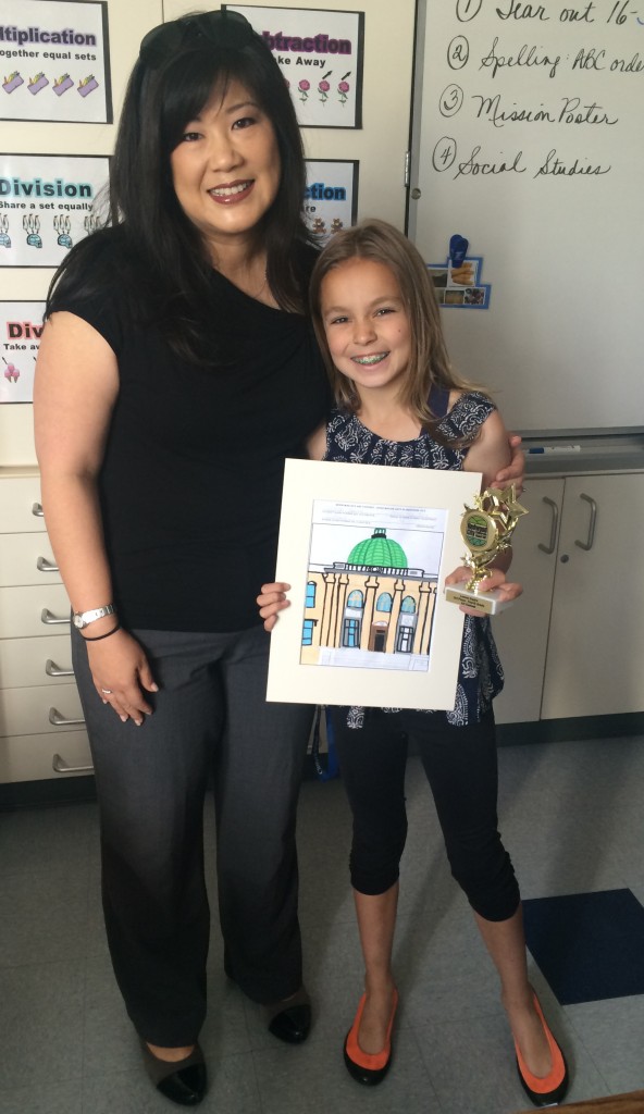 Art contest winner Lauren Squire smiles for the camera, holding her entry, beside Mrs. Behrendt, Principal